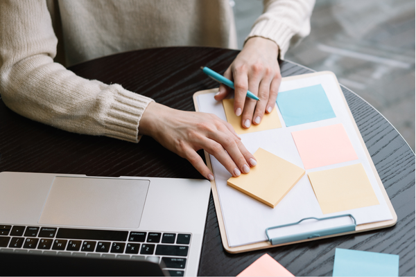 writing on sticky notes on a clipboard in front of laptop